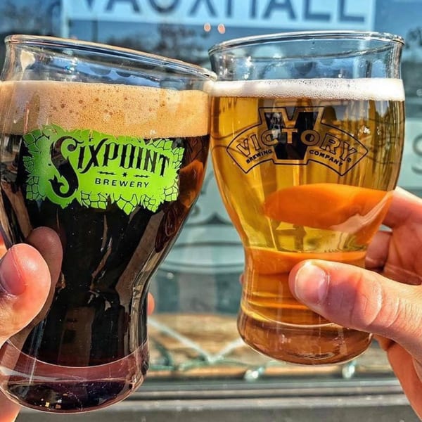Two hands holding glasses of dark and light beer, with brewery logos visible.