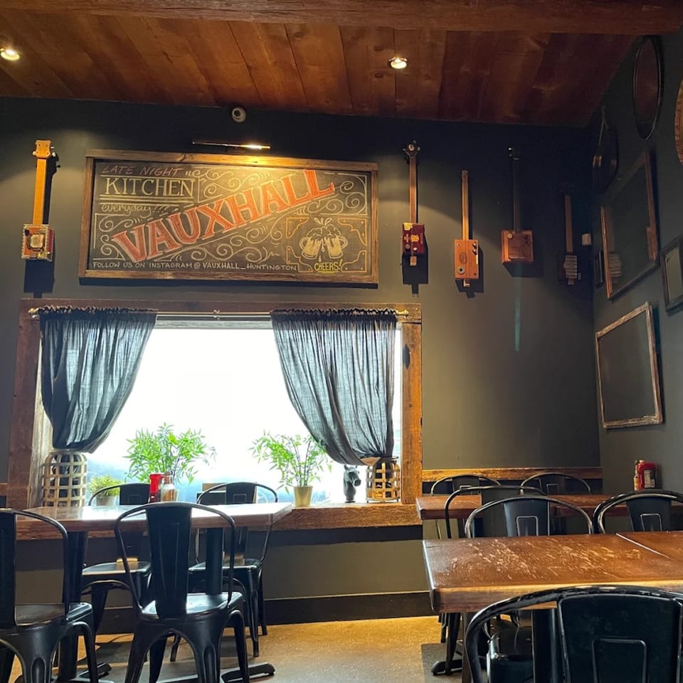 Interior of Vauxhall restaurant with wooden tables, black chairs, and a chalkboard sign on a dark wall.