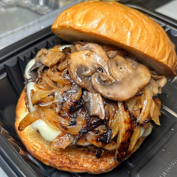 A Vauxhall burger with melted cheese, caramelized onions, and sautéed mushrooms on a toasted bun.