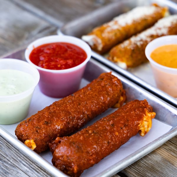 Vauxhall's mozzarella sticks and sauces on a metal tray, with two sauced sticks in the foreground.