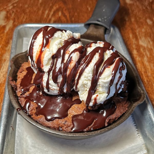 Warm chocolate chip cookie skillet topped with two scoops of vanilla ice cream and chocolate syrup.