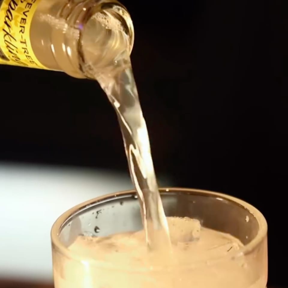 Sparkling beverage from a Fever-Tree bottle pours into a glass with ice.
