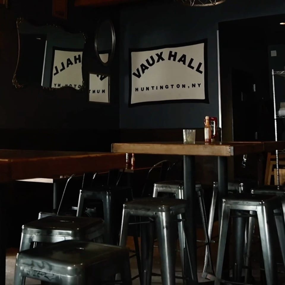 Interior of Vauxhall restaurant with a sign, bar stools, and wooden tables.