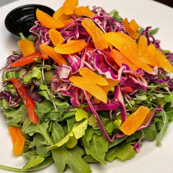 Vibrant salad with mixed greens, red cabbage, red peppers, and dried apricots on a white plate.