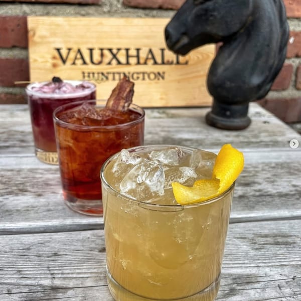 Three cocktails on a wooden table with a Vauxhall Huntington sign in the background.