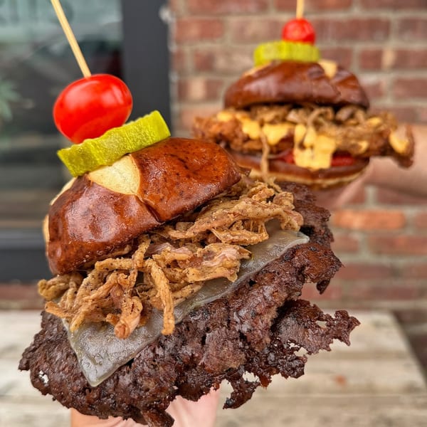 Two Vauxhall burgers with crispy onions, cheese, and a cherry tomato on a pretzel bun.